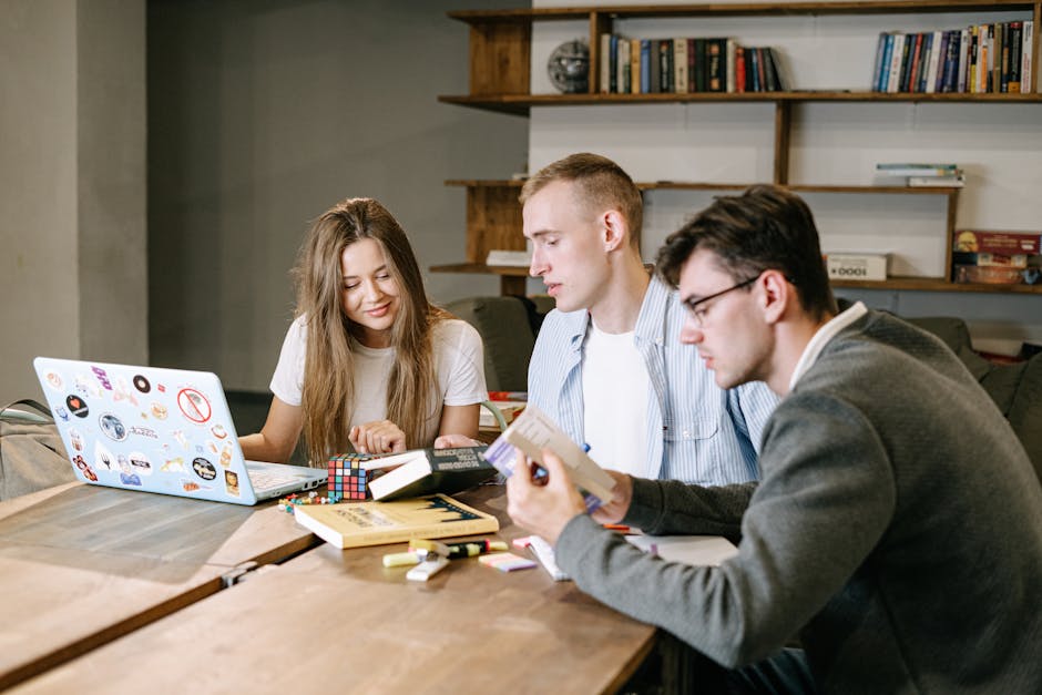 A group of young professionals collaborating on a project in a modern office space, working with books and a laptop
